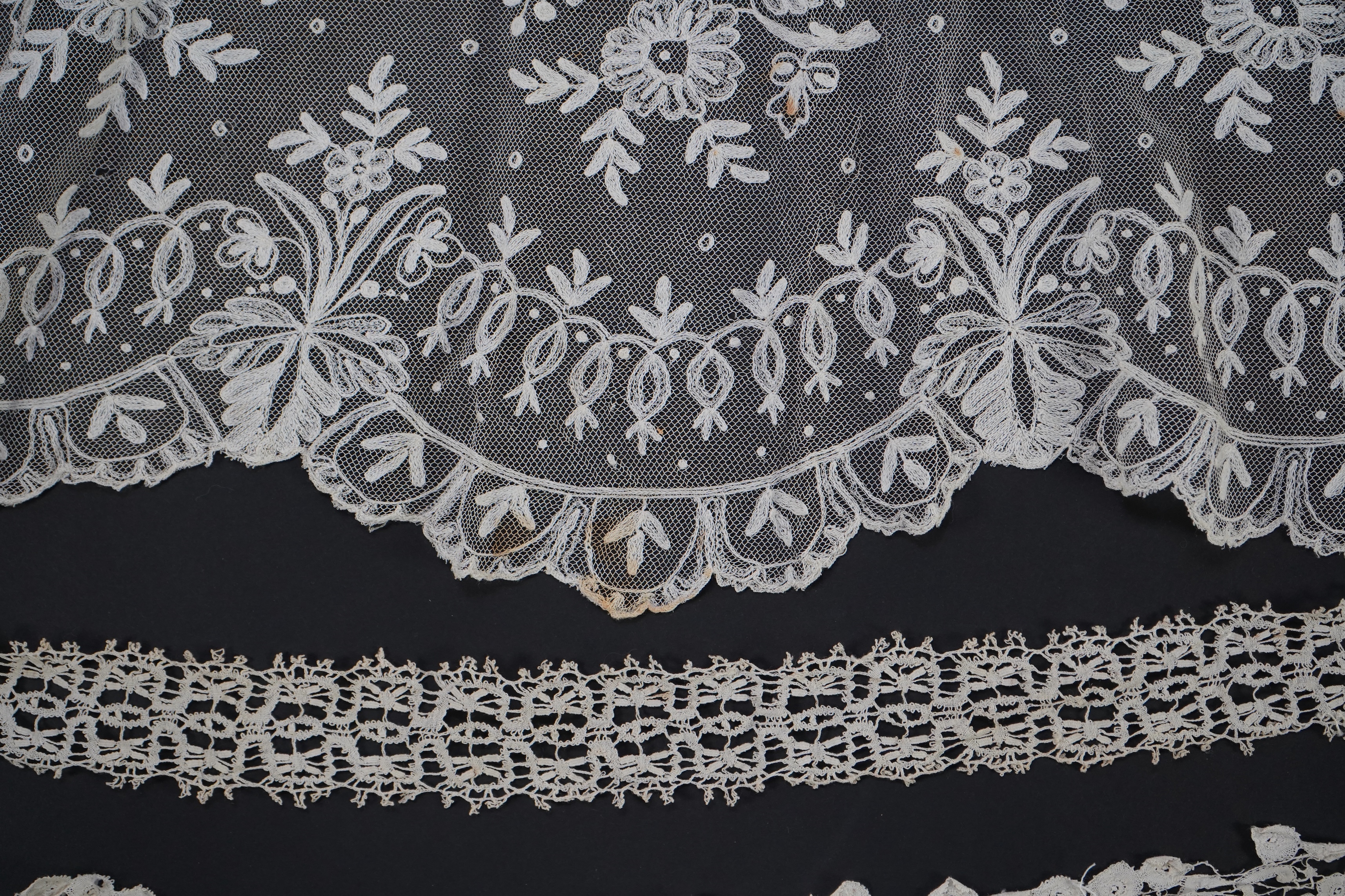 A white tape lace on net bed cover, a cream lace needle run panel, three Brussels bobbin lace collars, a lappet and two beaded tea pot covers, bed cover 200cm x 250cm. Condition - the bedcover has damage to the netting,